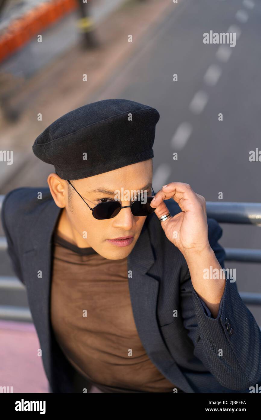 Latino gay mâle avec maquillage portant chapeau tendance posé sur un pont Banque D'Images