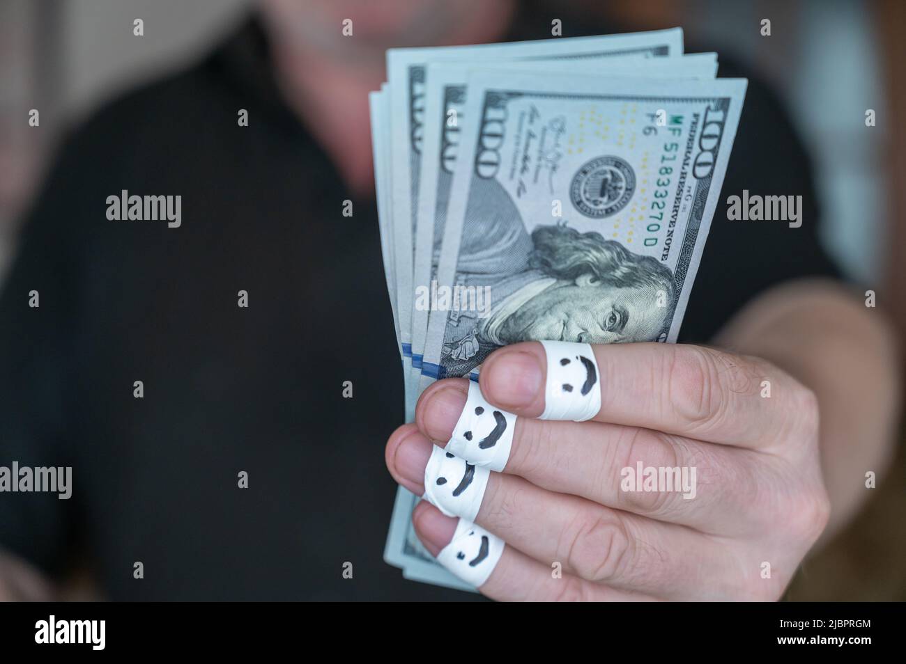 Un homme adulte tient sa main avec $100 billets à l'appareil photo. Les premières phalanges de ses doigts sont enveloppées dans un ruban blanc. Les visages souriants sont douloureux Banque D'Images