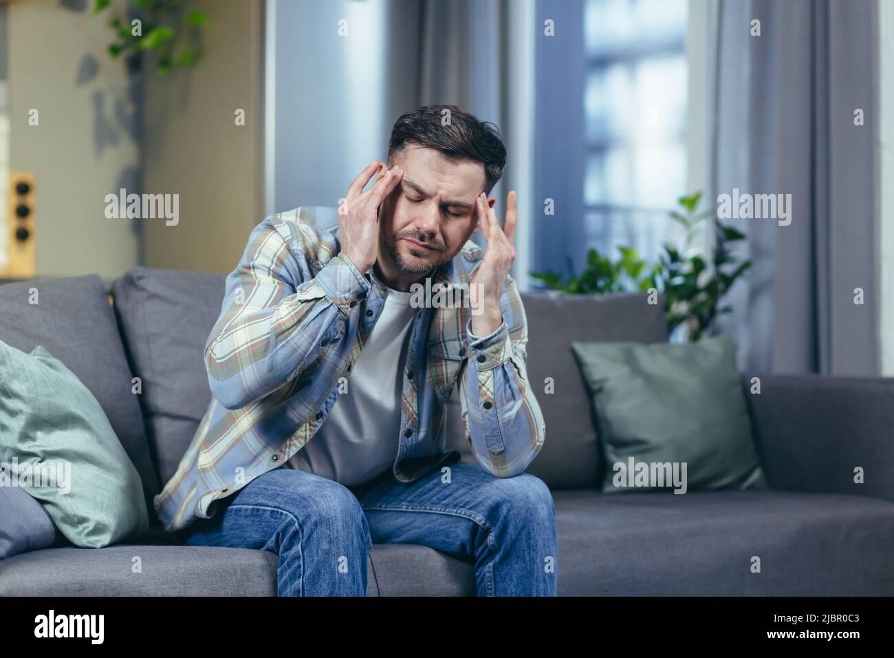 L'homme malade est assis seul à la maison sur le canapé, a un mal de tête sévère Banque D'Images