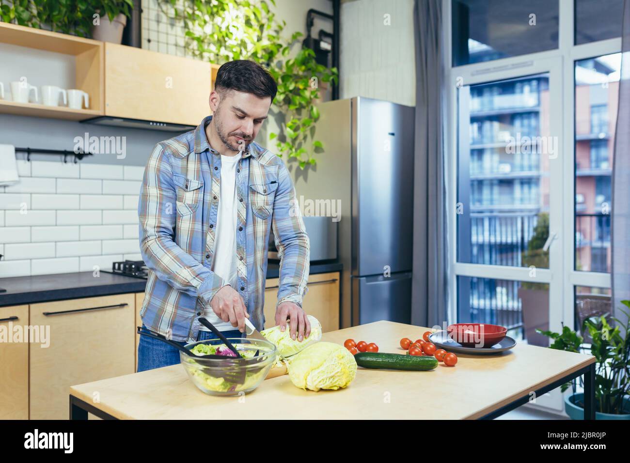 L'homme prépare des aliments sains et sains à la maison, coupe des légumes pour la salade dans la cuisine Banque D'Images