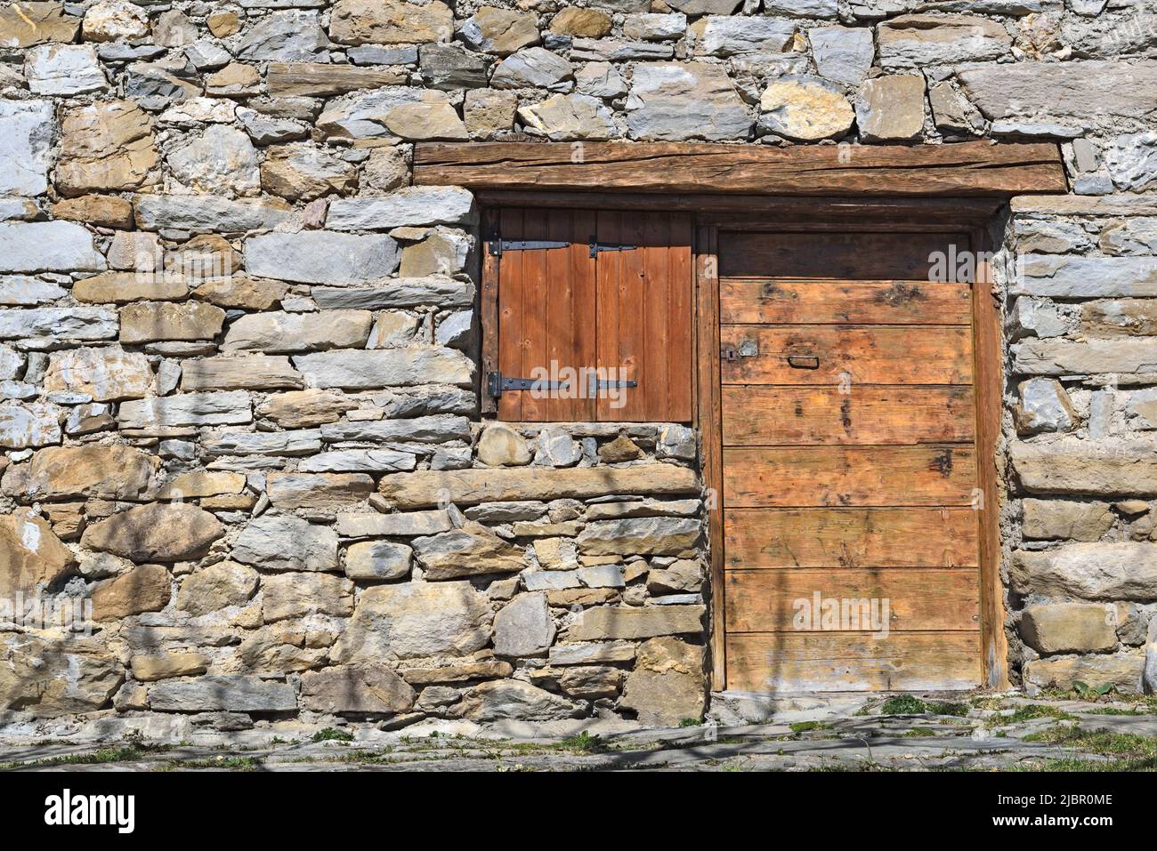 façade de l'ancien chalet alpin en pierre avec porte en bois et volets fermés Banque D'Images
