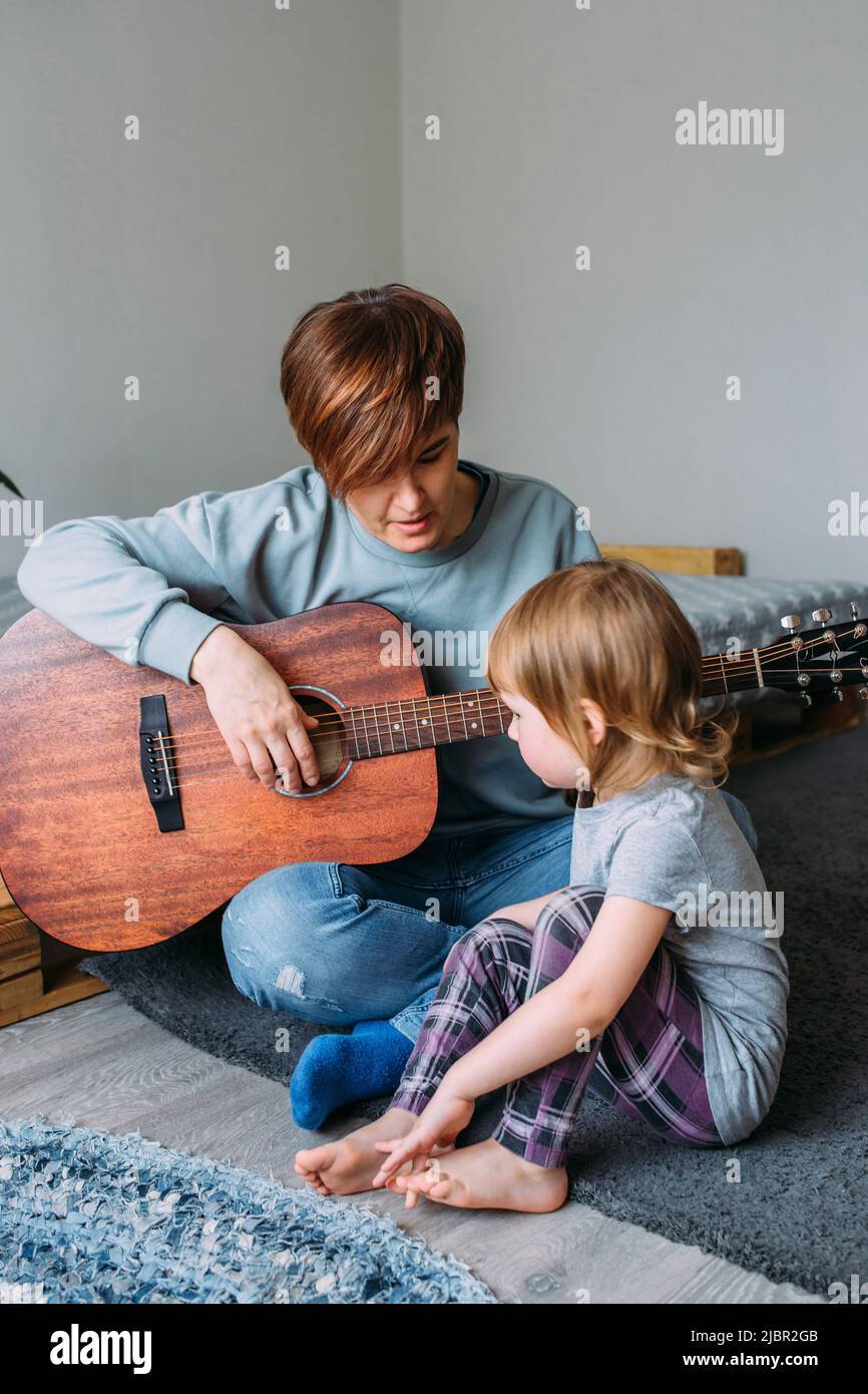 Une petite fille joue de la guitare avec sa mère sur le sol à la maison Banque D'Images