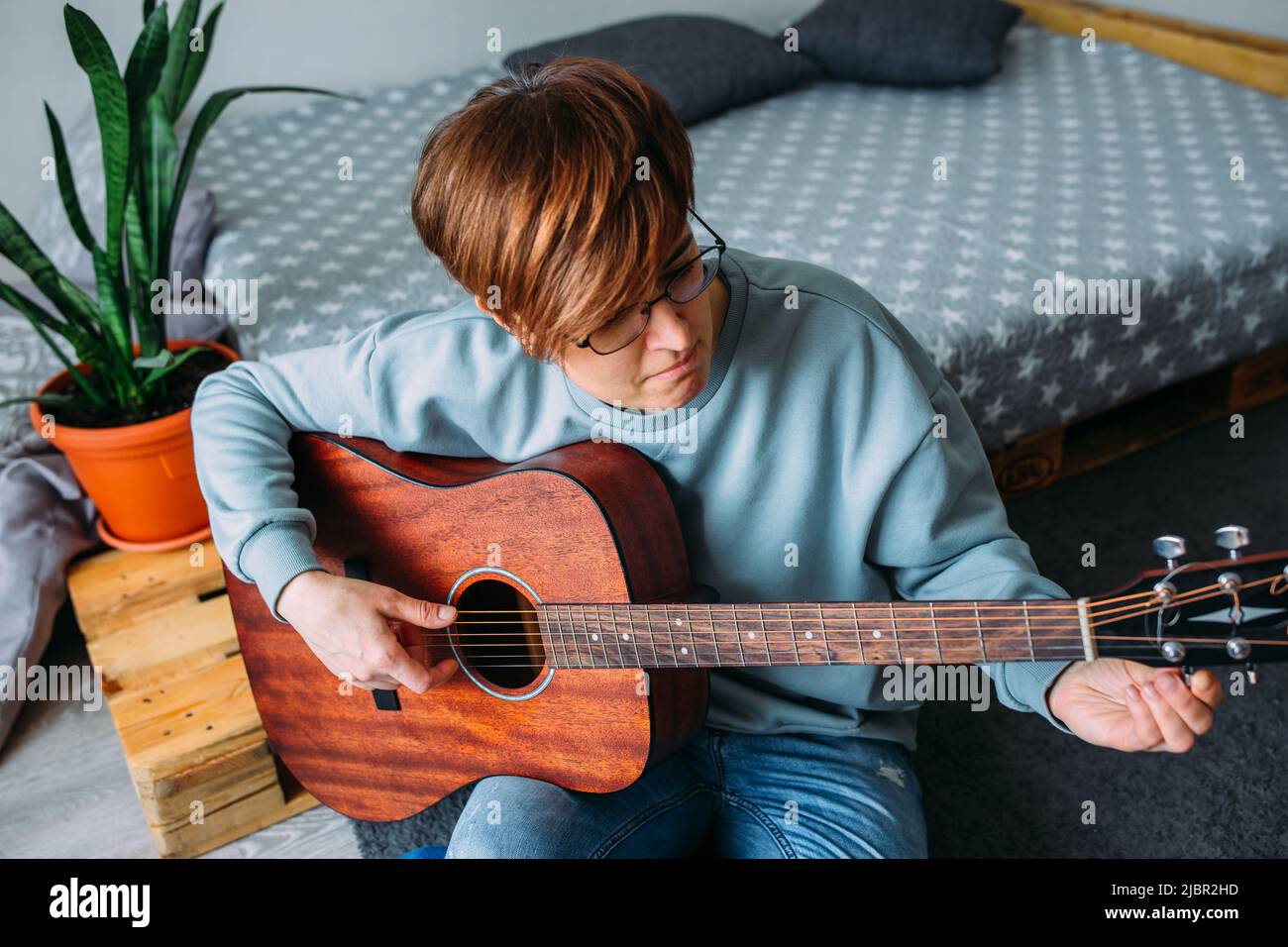 Femme aux cheveux courts aime jouer de la guitare à la maison. Leçons de musique pour adultes Banque D'Images