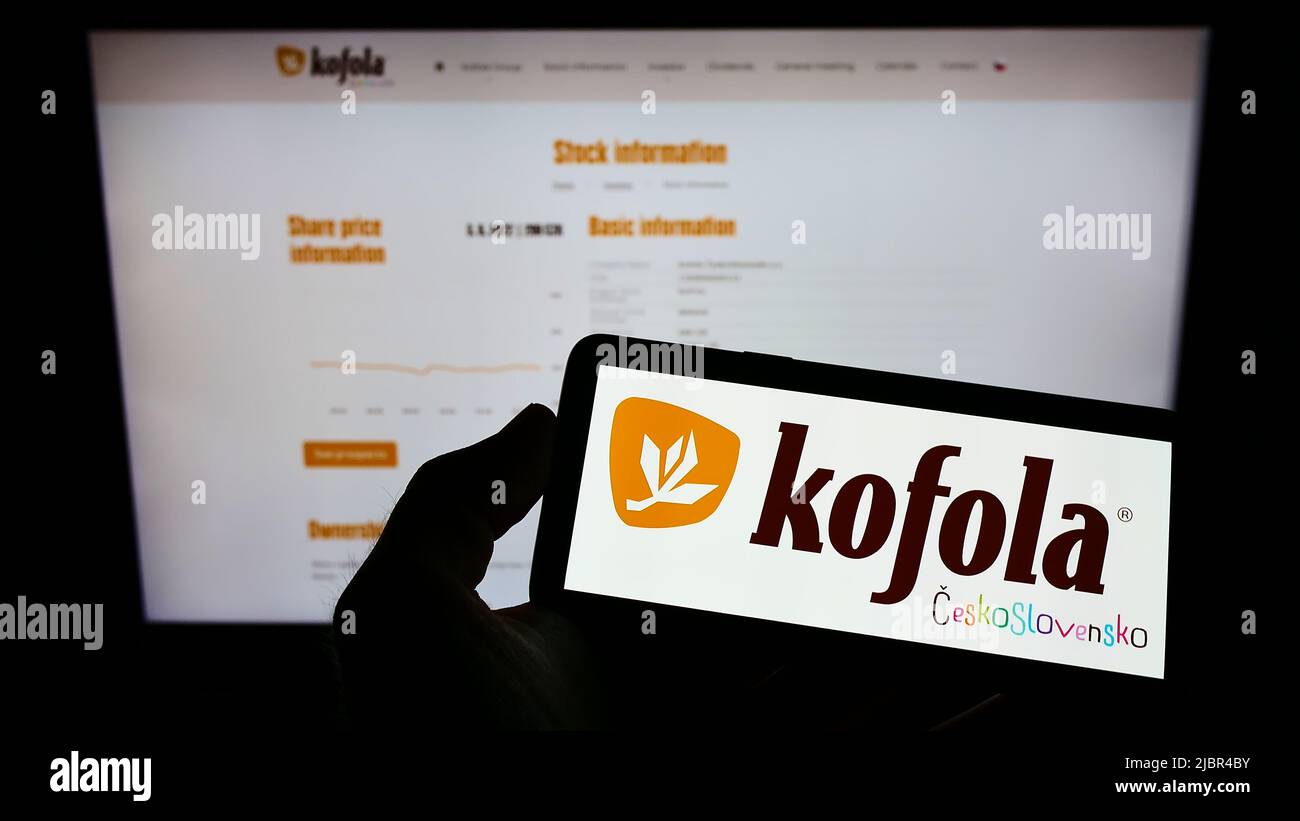 Personne tenant un téléphone portable avec le logo de la société tchèque Kofola CeskoSlovensko a.s. à l'écran en face de la page web d'affaires. Mise au point sur l'affichage du téléphone. Banque D'Images