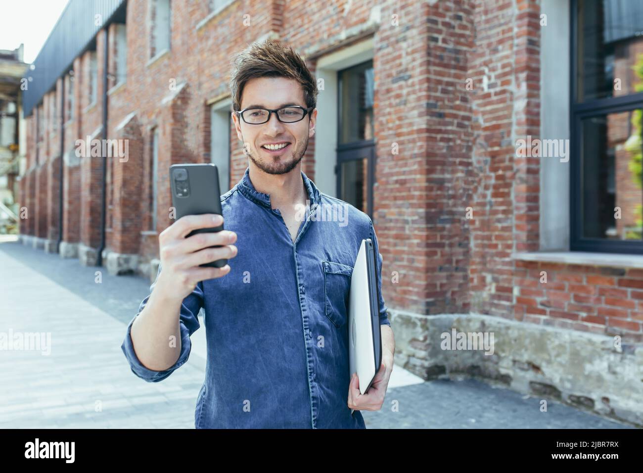 Un jeune homme d'affaires utilise le téléphone à l'extérieur du bureau, un homme heureux et souriant avec un smartphone Banque D'Images