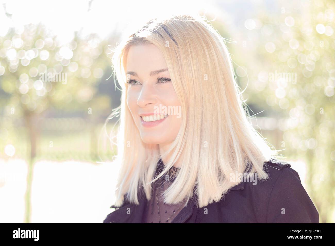 jolie femme blonde souriante dans un parc habillé de noir Banque D'Images