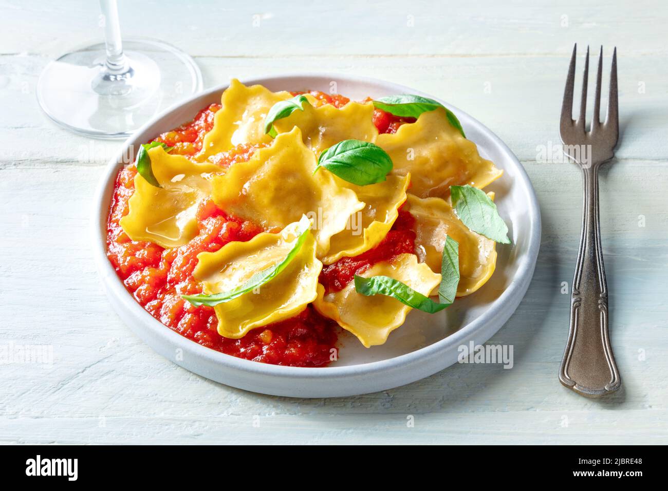 Raviolis à la sauce tomate et feuilles de basilic frais sur une assiette, dîner italien, sur une table en bois avec un verre de vin Banque D'Images