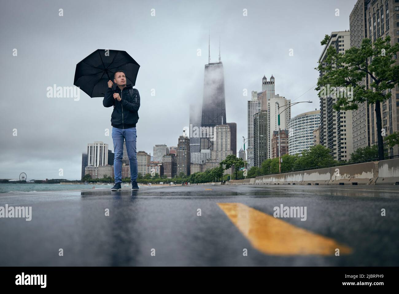 Jour pluvieux et venteux en ville. Homme avec un parapluie marchant contre le paysage urbain de Chicago. Banque D'Images