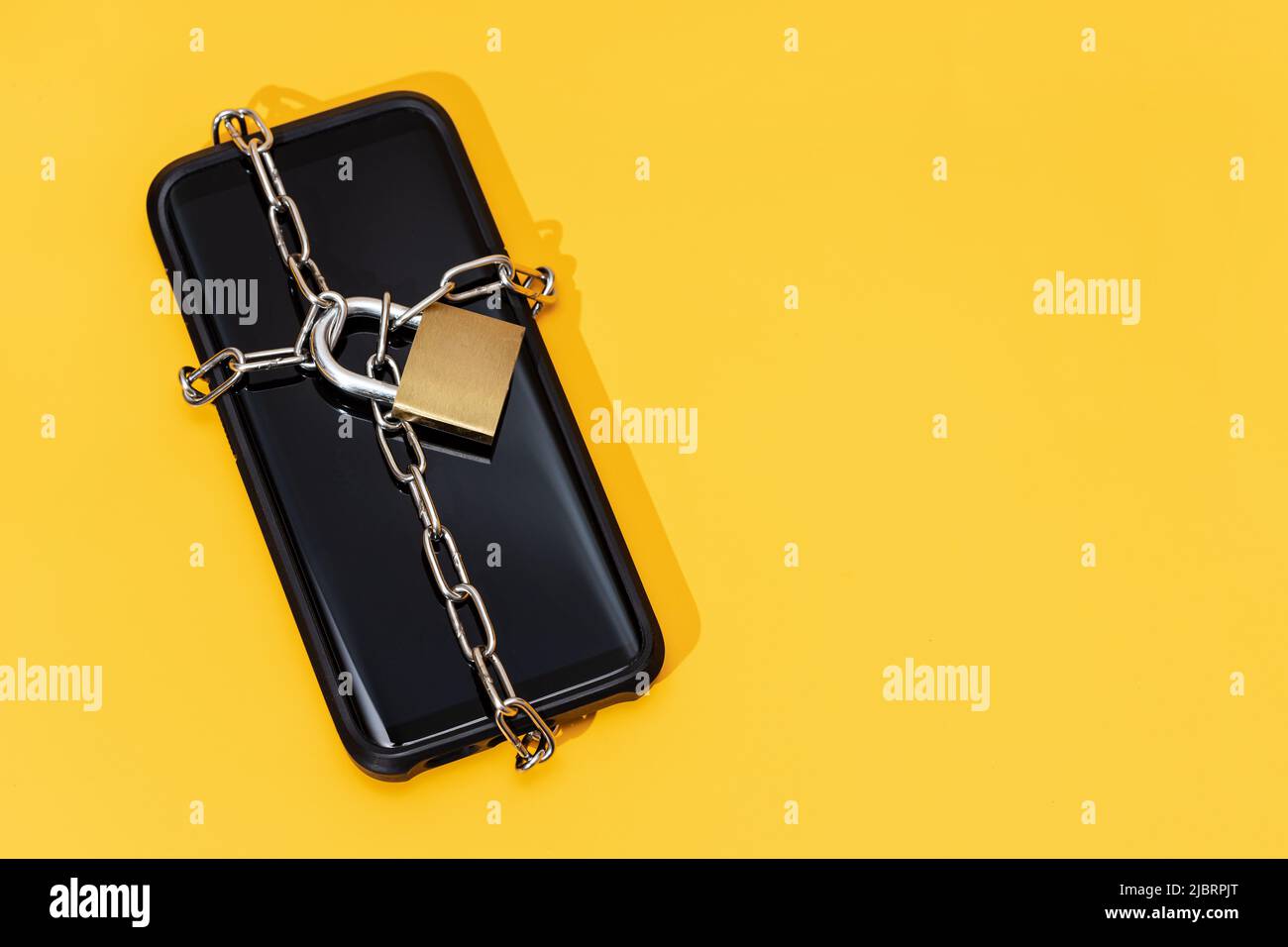 Concept de sécurité du téléphone. Smartphone verrouillé avec chaîne et cadenas sur fond jaune. Sécurité mobile et confidentialité des données. Copier l'espace Banque D'Images