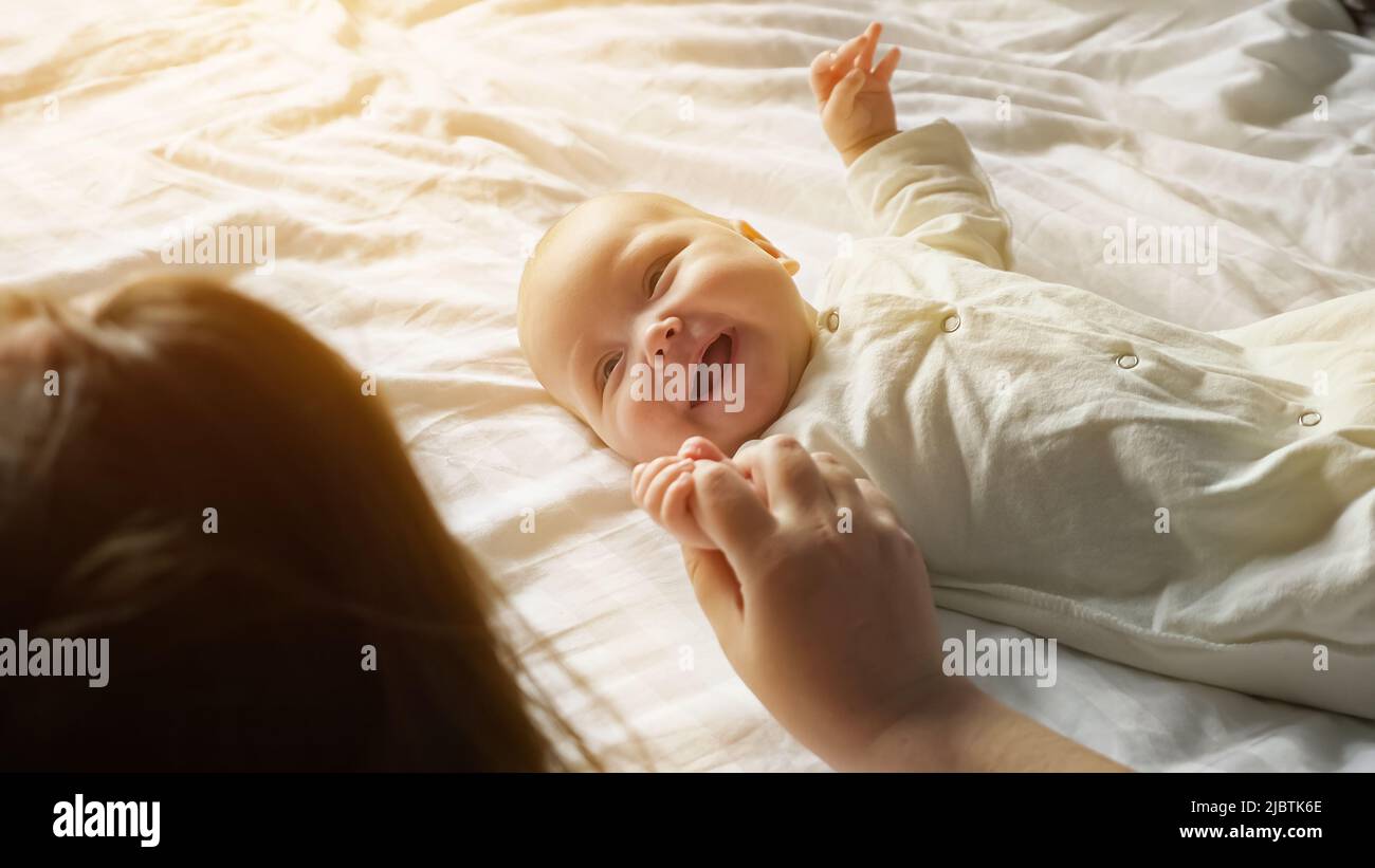 Bébé souriant repose sur un drap blanc qui attire l'attention de sa mère Banque D'Images