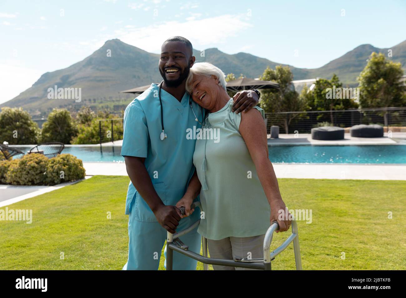 Travailleur de la santé afro-américain qui embrasse une femme de race blanche avec un cadre de marche dans le jardin Banque D'Images