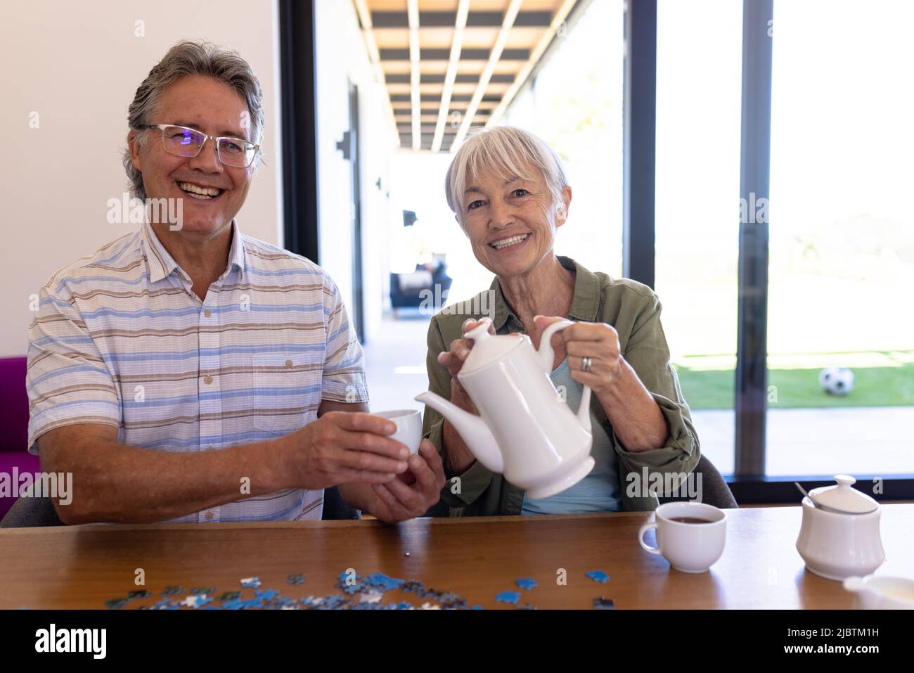 Portrait d'une femme asiatique âgée souriante qui verse du café dans une tasse, tenue à table par un homme de race blanche Banque D'Images
