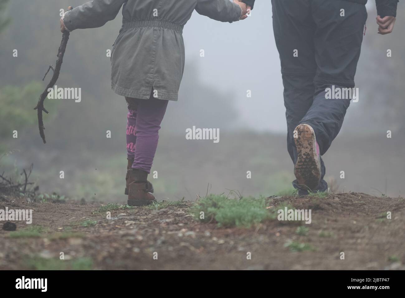 Mise au point sélective des pieds arrière de la mère et de la fille avec le bâton marchant dans le champ par temps brumeux. Étape par étape dans la nature. Banque D'Images