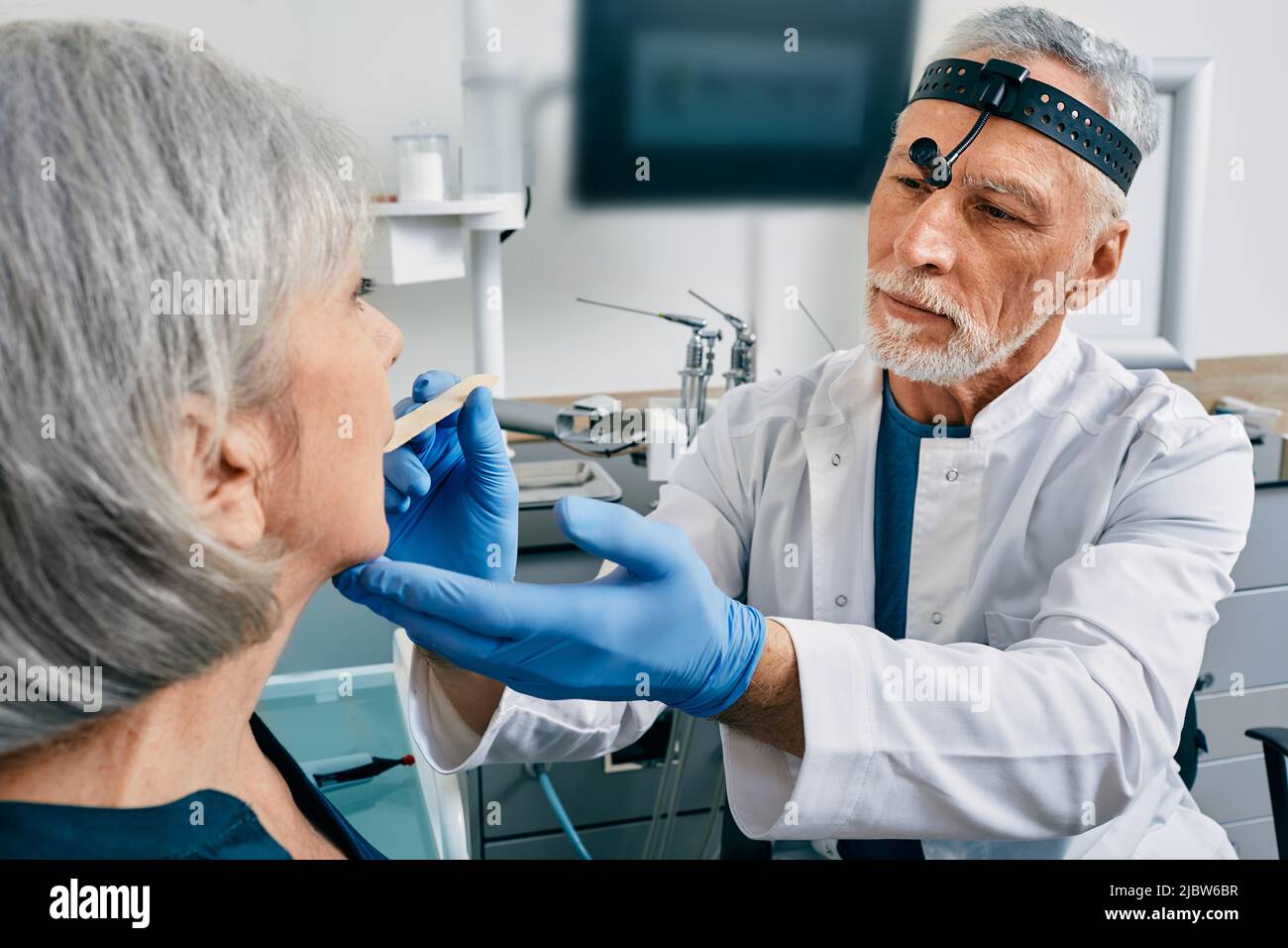 médecin utilisant la spatule d'inspection examine la gorge de la femme âgée. Consultation ORL, examen de la gorge Banque D'Images