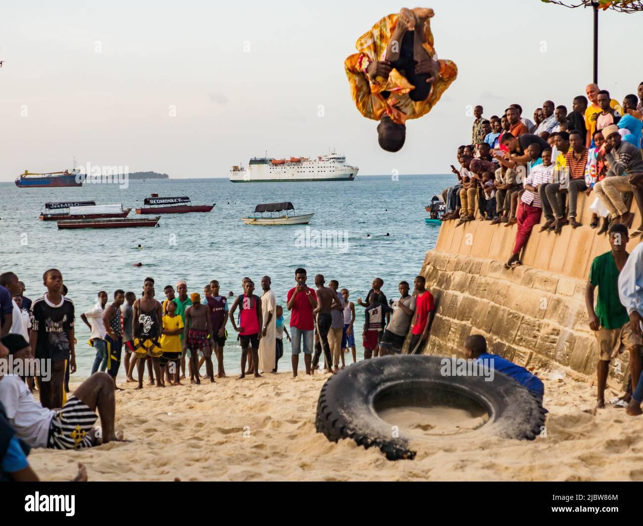 Stone Town, Zanzibar, Tanzanie - janvier 2021: Des foules de gens regardent comme des jeunes sauter sur un tube intérieur sur une plage de sable de Stone Town. Afrique Banque D'Images