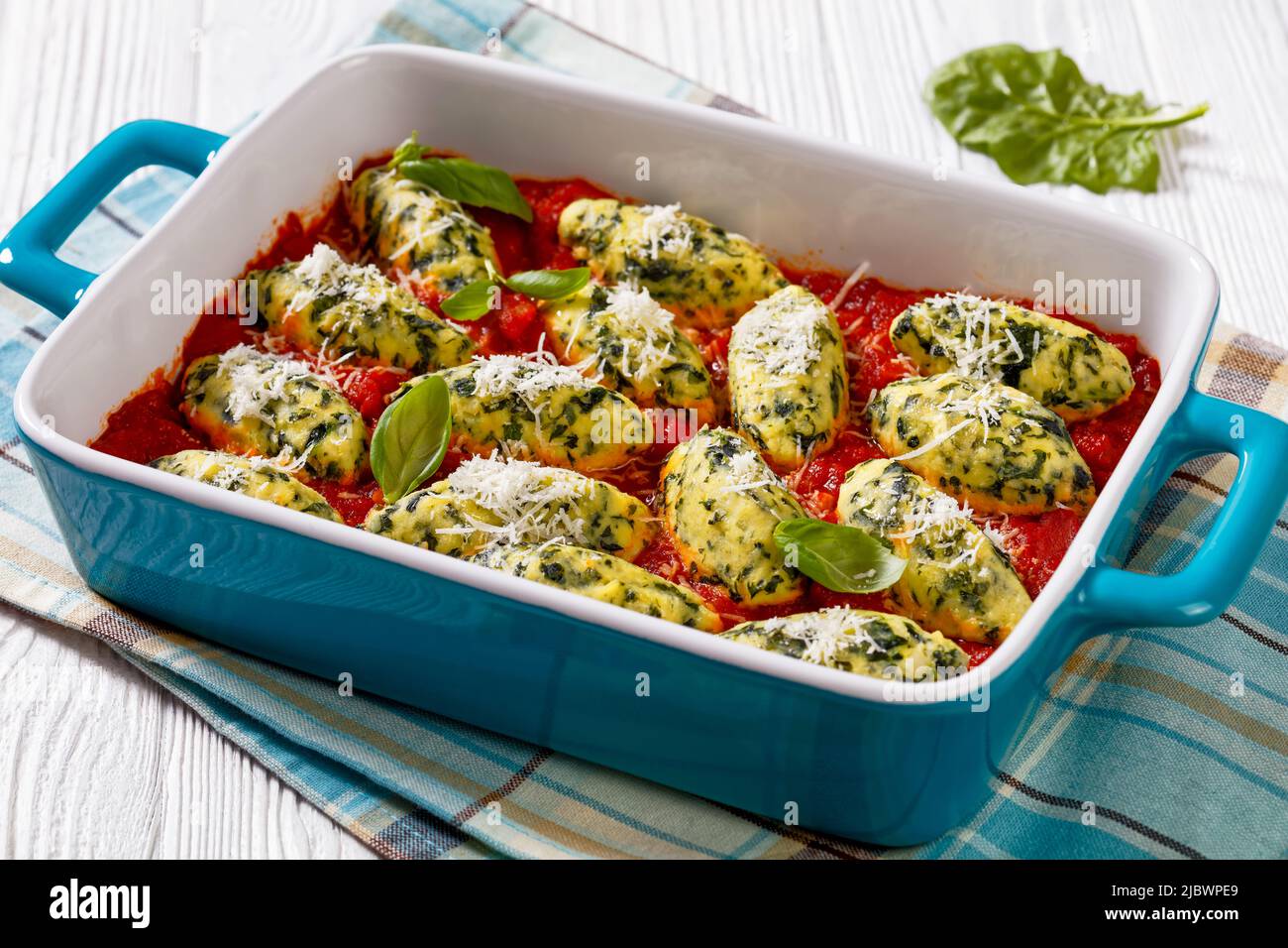Boulettes de ricotta aux épinards italiens dans une sauce tomate aux herbes et parmesan râpé dans un plat de cuisson en céramique sur une table blanche Banque D'Images