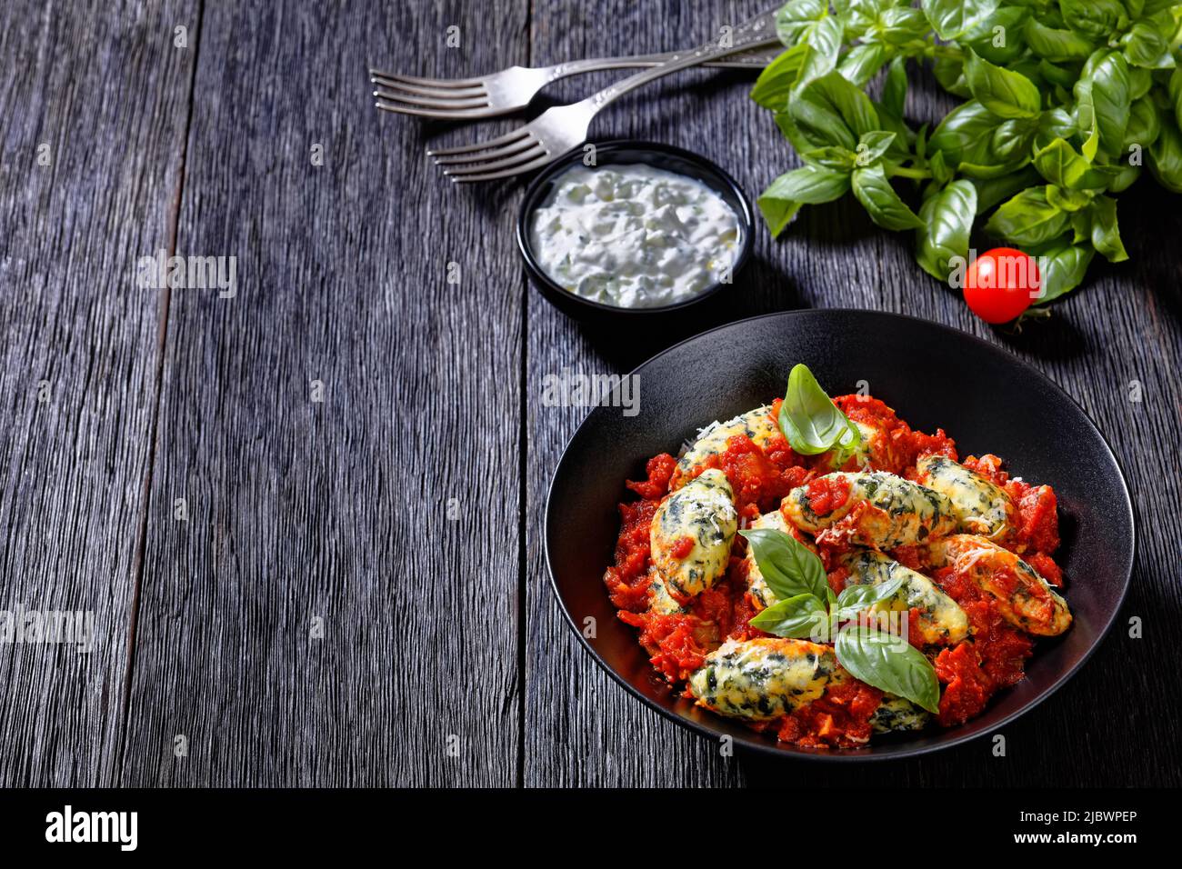 Boulettes de ricotta aux épinards italiens sauce tomate aux herbes et parmesan râpé dans un bol noir sur une table en bois sombre, vue horizontale Banque D'Images