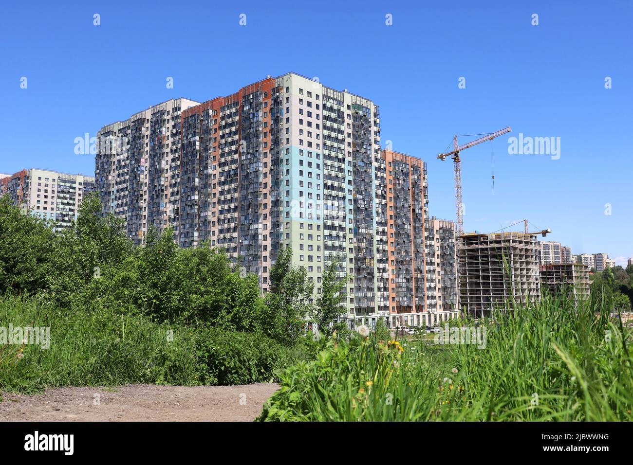 Vue sur les nouveaux bâtiments résidentiels, la grue de construction et les arbres verts. Immobilier en été Banque D'Images