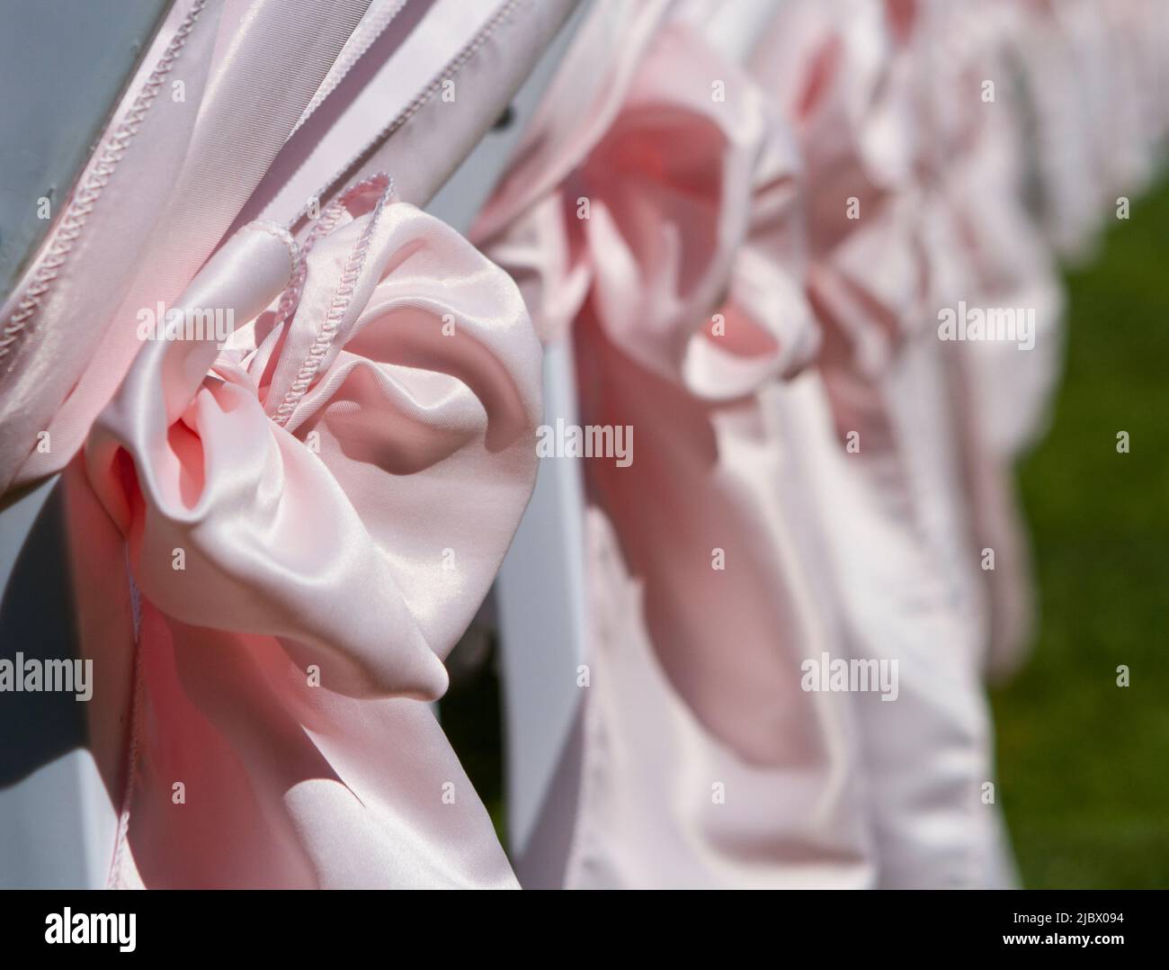 Rangée de chaises blanches avec de grands rubans roses prêts pour un mariage d'été en plein air. Banque D'Images