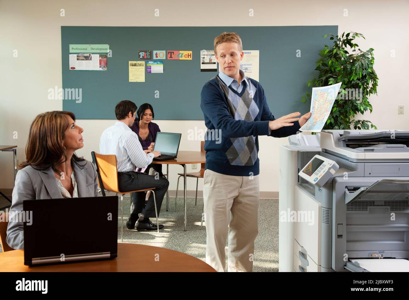 Homme au photocopieur parlant avec une collègue sur un ordinateur portable Banque D'Images