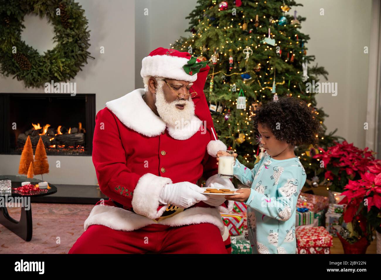 Jolie jeune fille qui distribue du lait et des biscuits du Père Noël devant l'arbre de Noël Banque D'Images