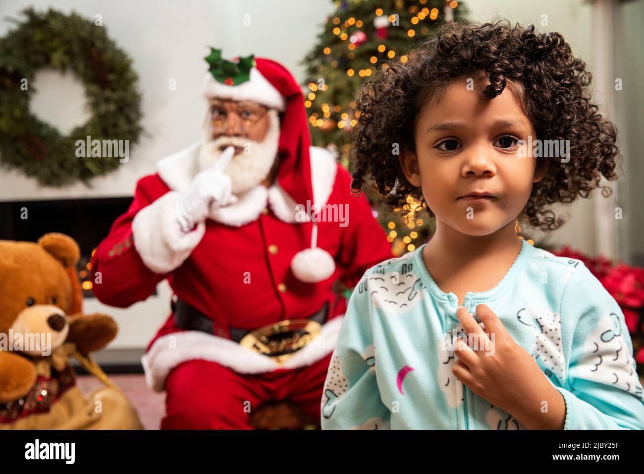 Jeune fille regardant dans l'appareil photo avec son grand-père habillé comme le Père Noël en arrière-plan. Noël amusant. Banque D'Images