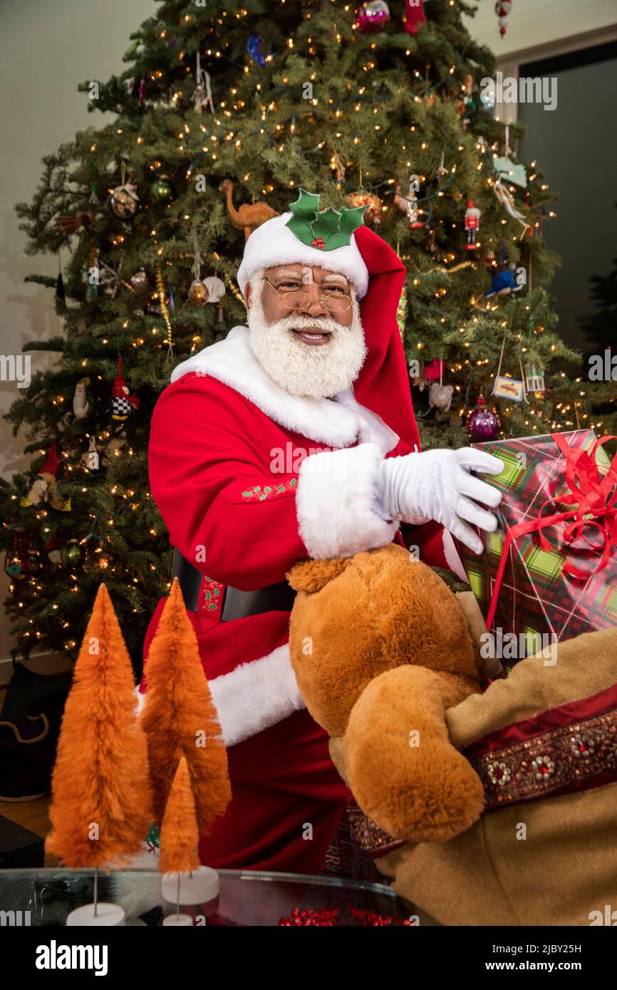 Le Père Noël tire les cadeaux de son sac de jouets et les place sous l'arbre de Noël. Série Père Noël noir. Banque D'Images