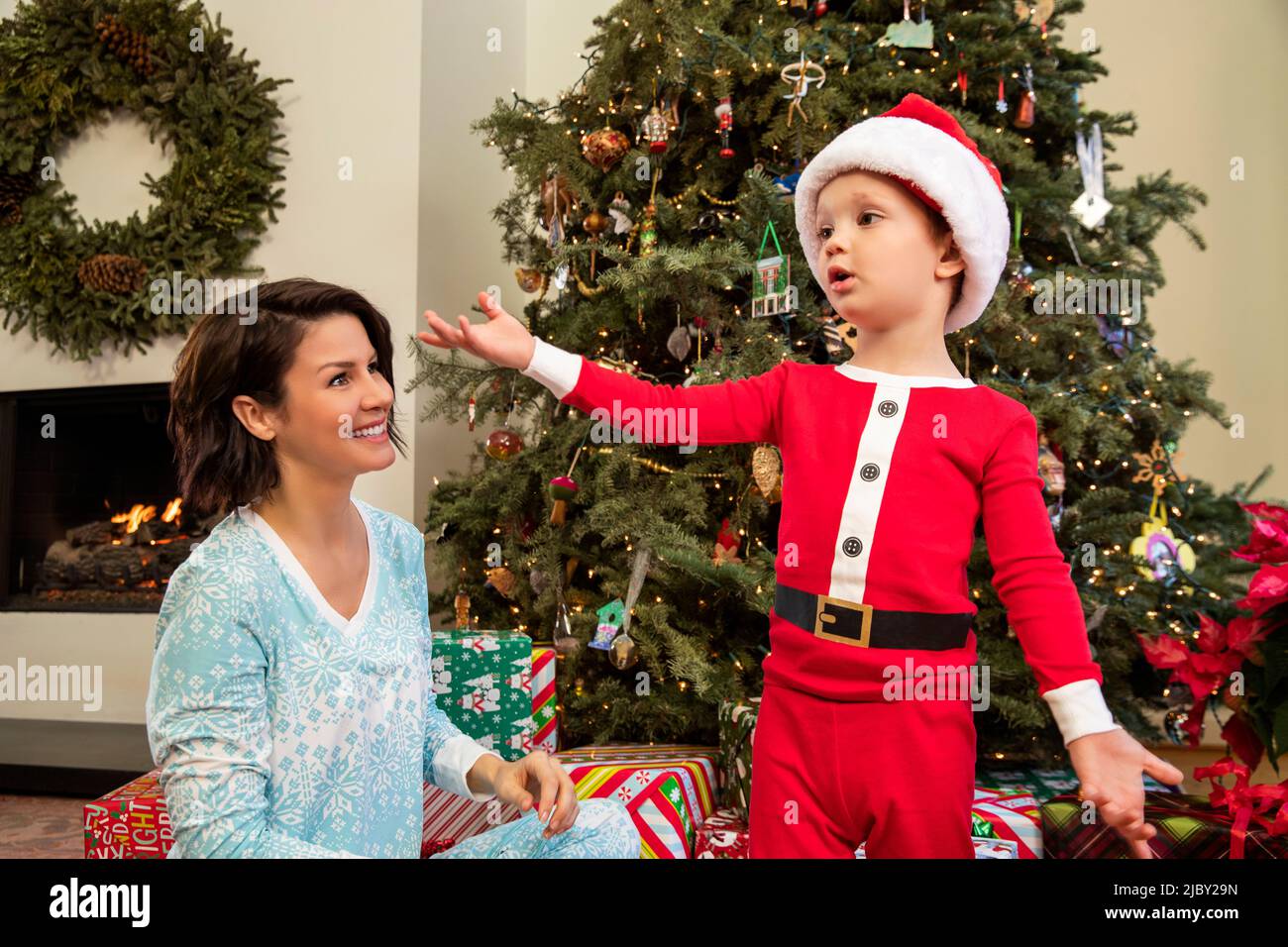 Garçon en pyjama du Père Noël debout devant l'arbre de Noël avec la mère. Banque D'Images