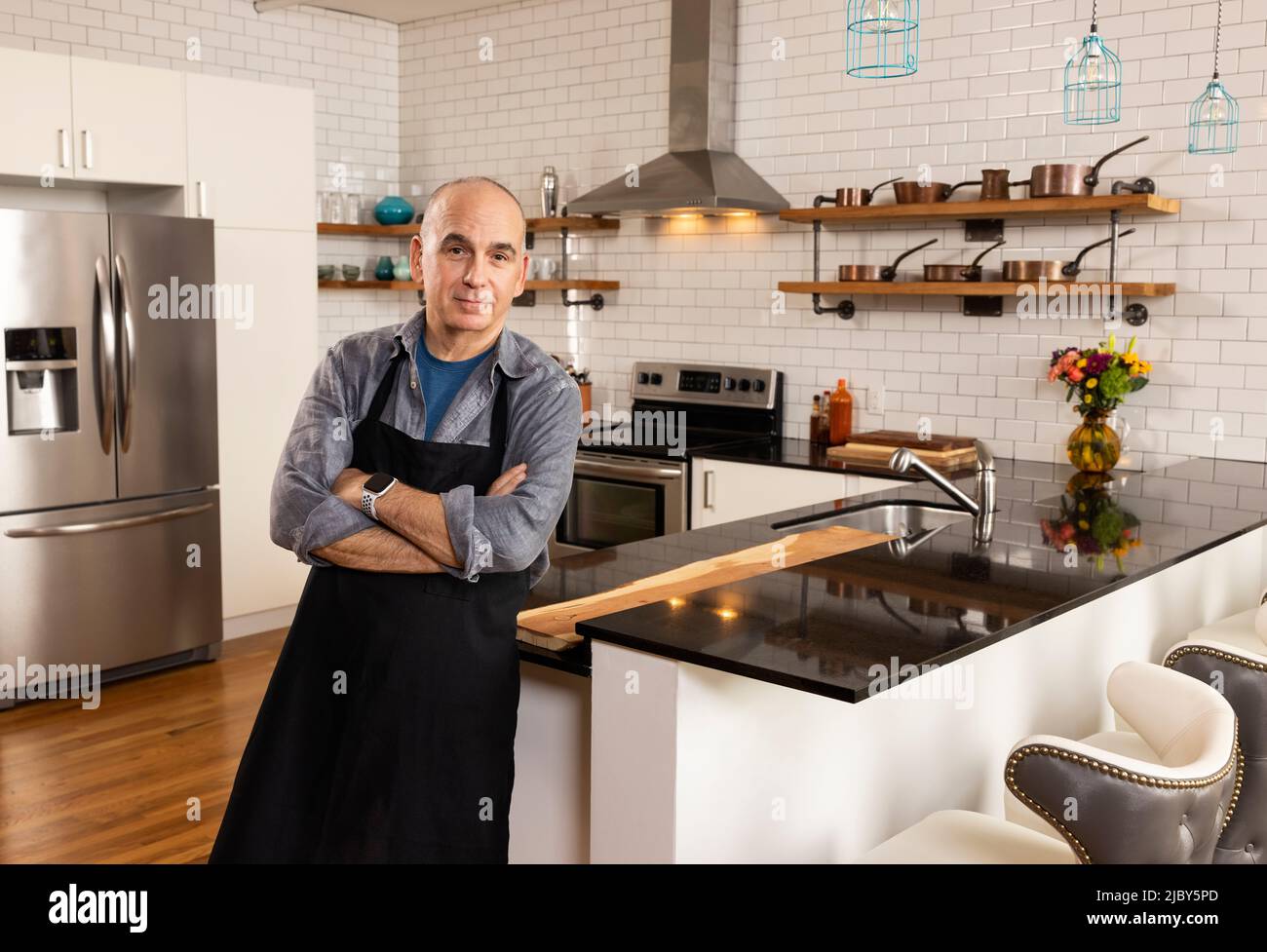 Homme s'inclinant contre le comptoir de la cuisine avec les bras croisés regardant dans l'appareil photo. Banque D'Images