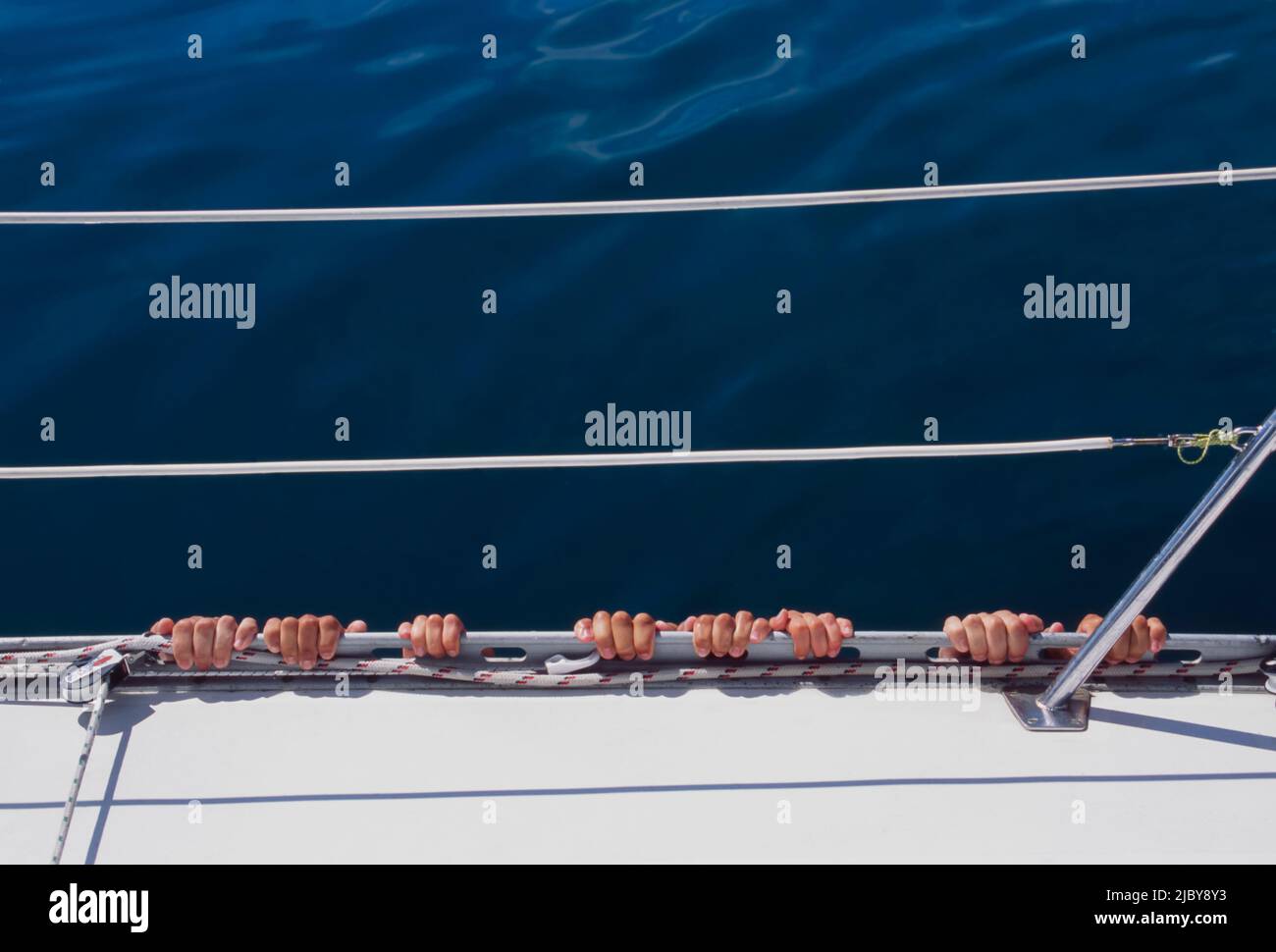 Quatre ensembles de doigts accrochés sur le côté du yacht dans l'eau calme Banque D'Images