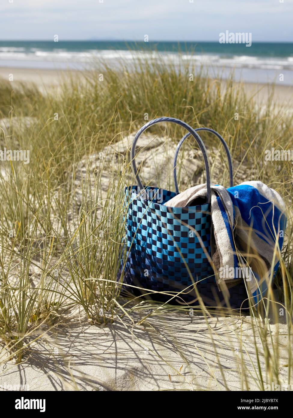 Sac et serviette assis sur une dune de sable herbacée à la plage Banque D'Images