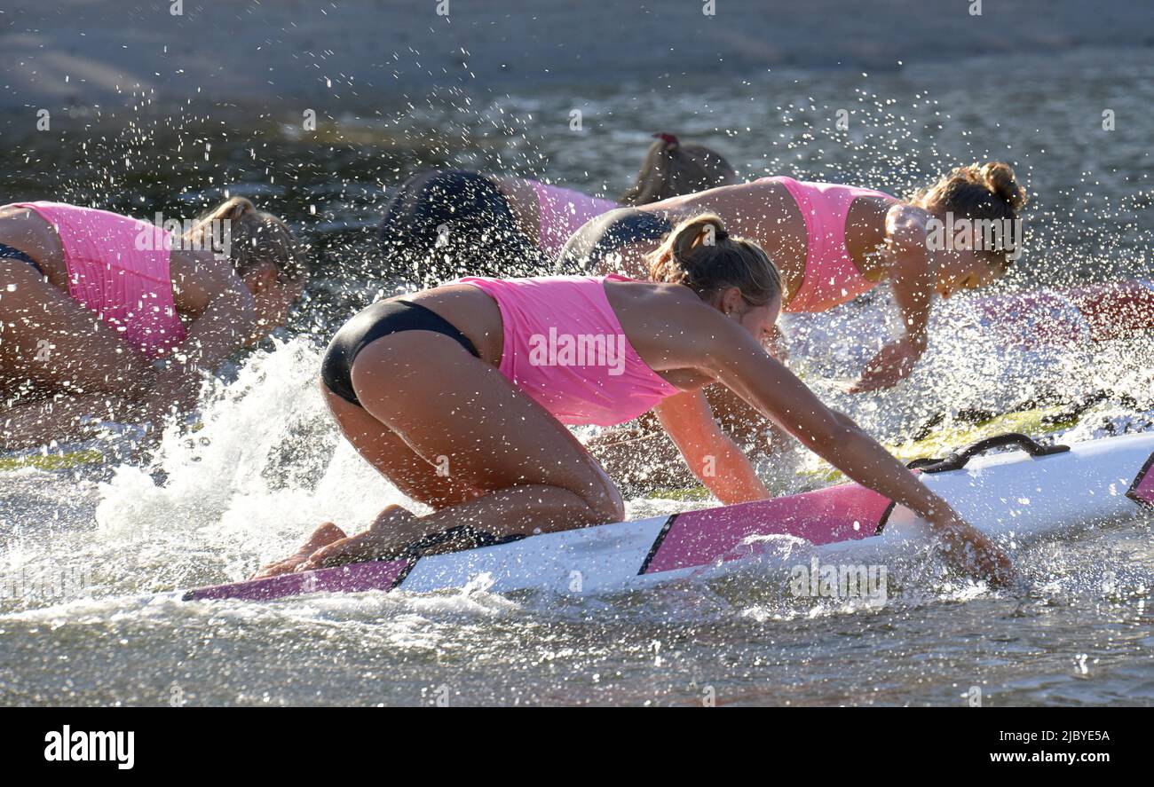 Vue latérale de l'équipe de sauveteurs de surf de sexe féminin s'entraîner et pagayer à plat sur les planches Banque D'Images