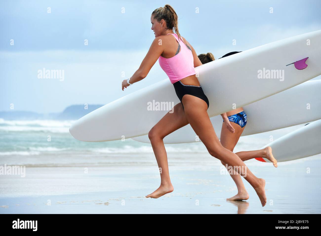 Vue latérale de l'équipe de sauveteurs de surf féminins s'entraîner et courir dans la mer tenant des skis de surf de l'océan Banque D'Images