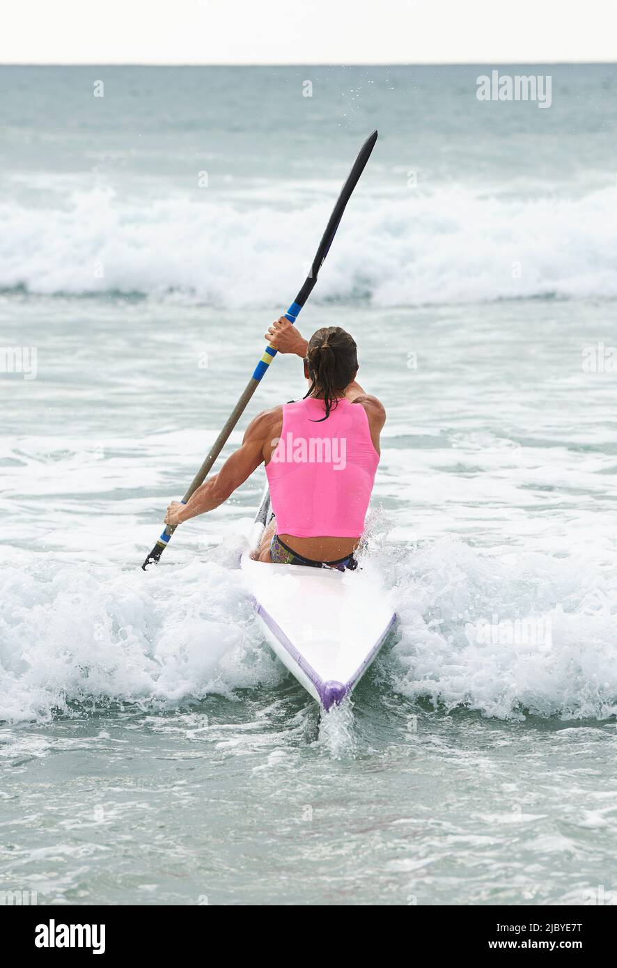 Vue arrière de la femme surf sauvetage pagayer à travers les vagues sur l'océan surf ski Banque D'Images