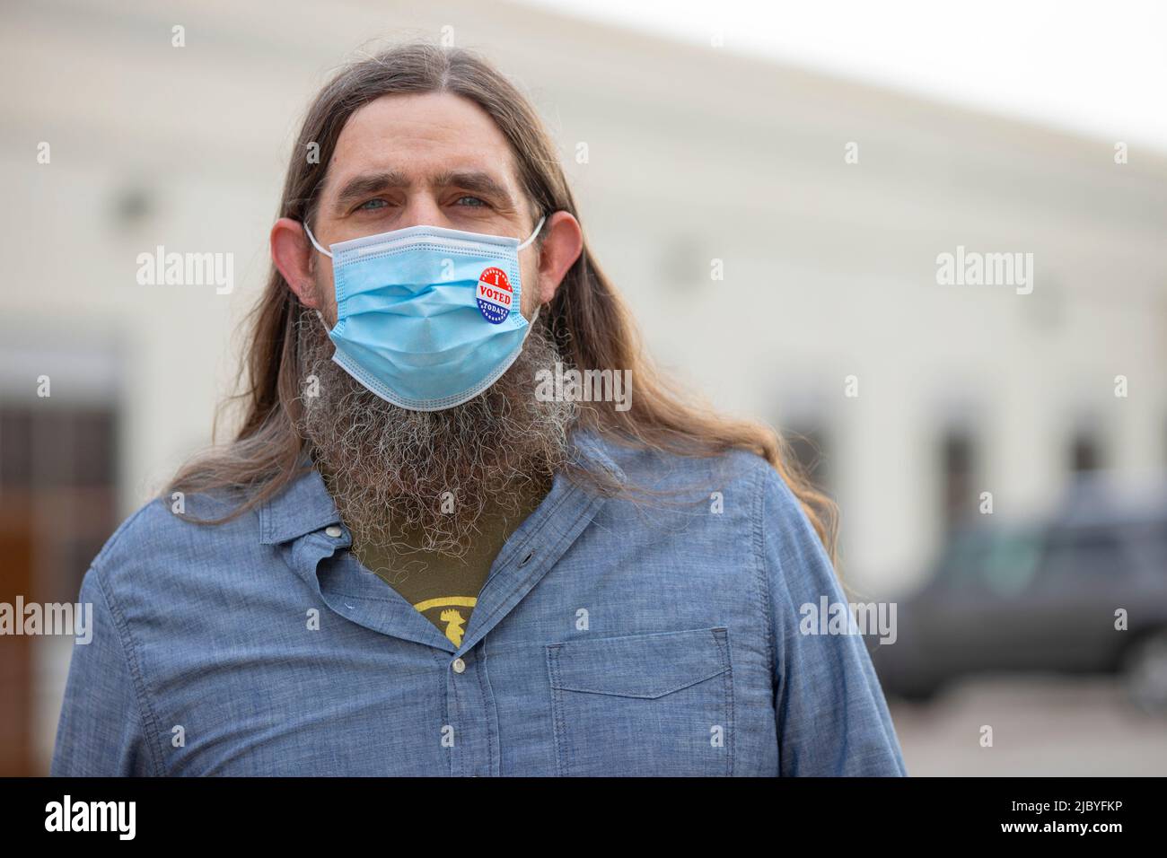 Homme caucasien avec de longs cheveux et une barbe complète portant un masque et un autocollant J'ai voté aujourd'hui sur le masque, regardant dans l'appareil photo. Banque D'Images