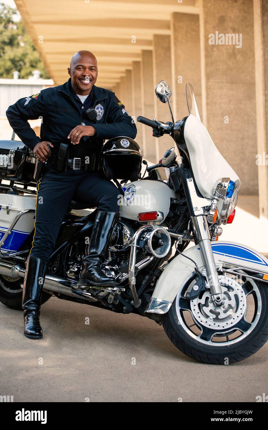 Portrait de l'officier de police assis sur sa moto à l'extérieur en regardant vers la caméra souriante Banque D'Images