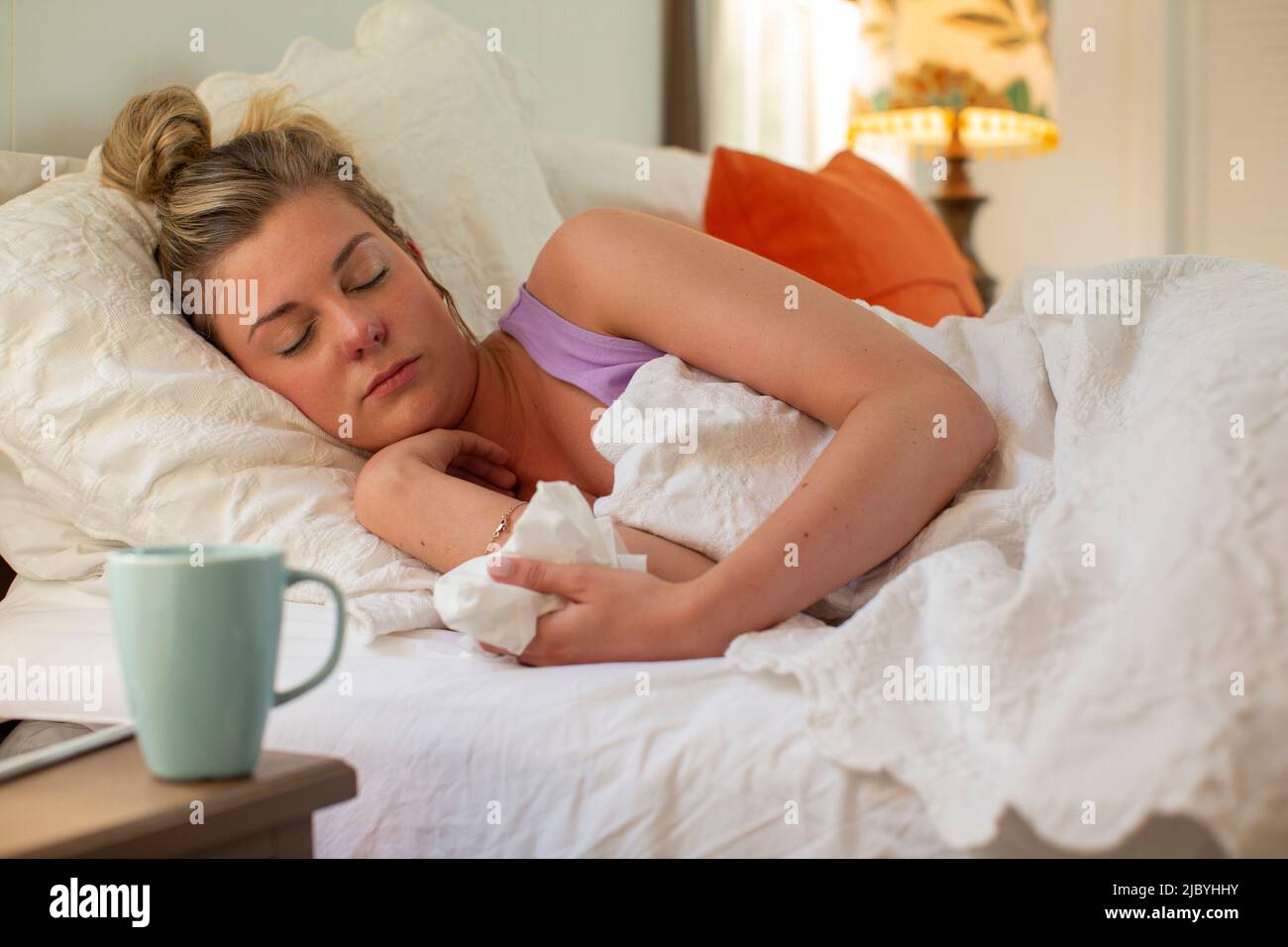 Une jeune femme dormant dans son lit, tenant le papier de soie à la main, un smartphone et une tasse à café assis sur une table de chevet Banque D'Images