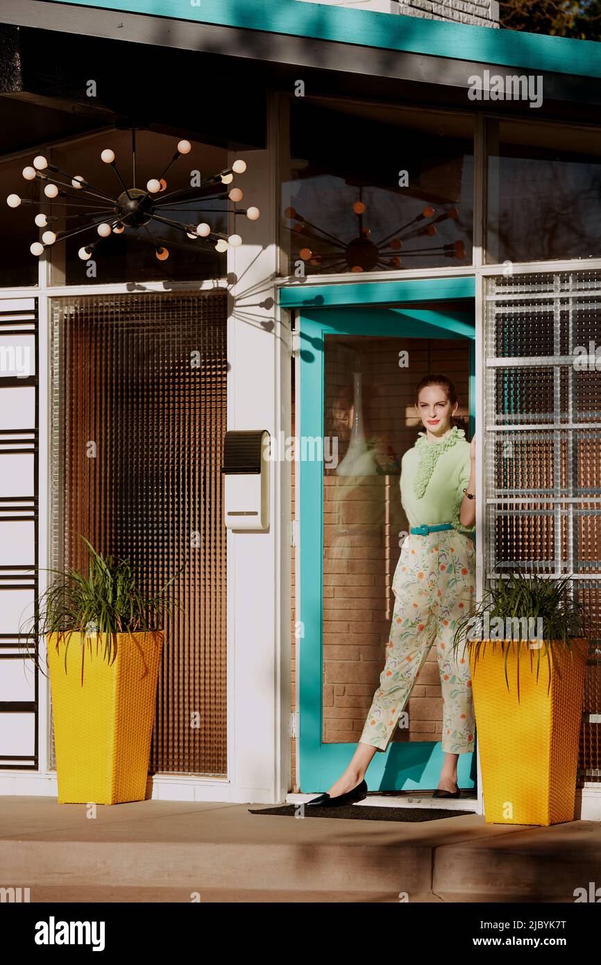 Portrait contemporain sur le thème vintage d'une femme debout dans une porte d'entrée d'une maison de style du milieu du siècle. Banque D'Images