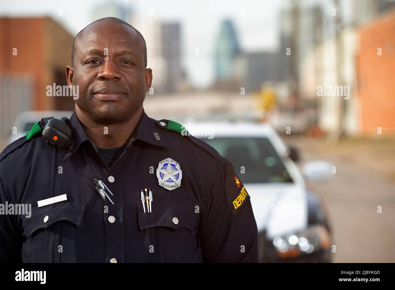 Portrait de l'officier de police debout dans la rue devant la voiture de l'escouade regardant vers la caméra avec les bras derrière son dos Banque D'Images