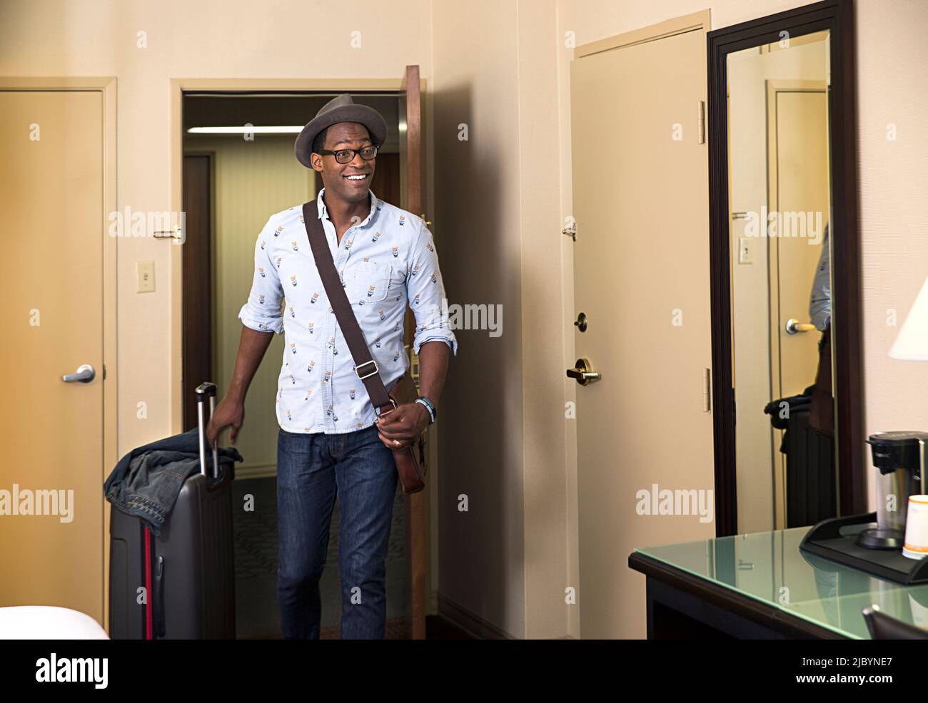 Homme noir avec rolling suitcase entrant dans chambre d'hôtel Banque D'Images