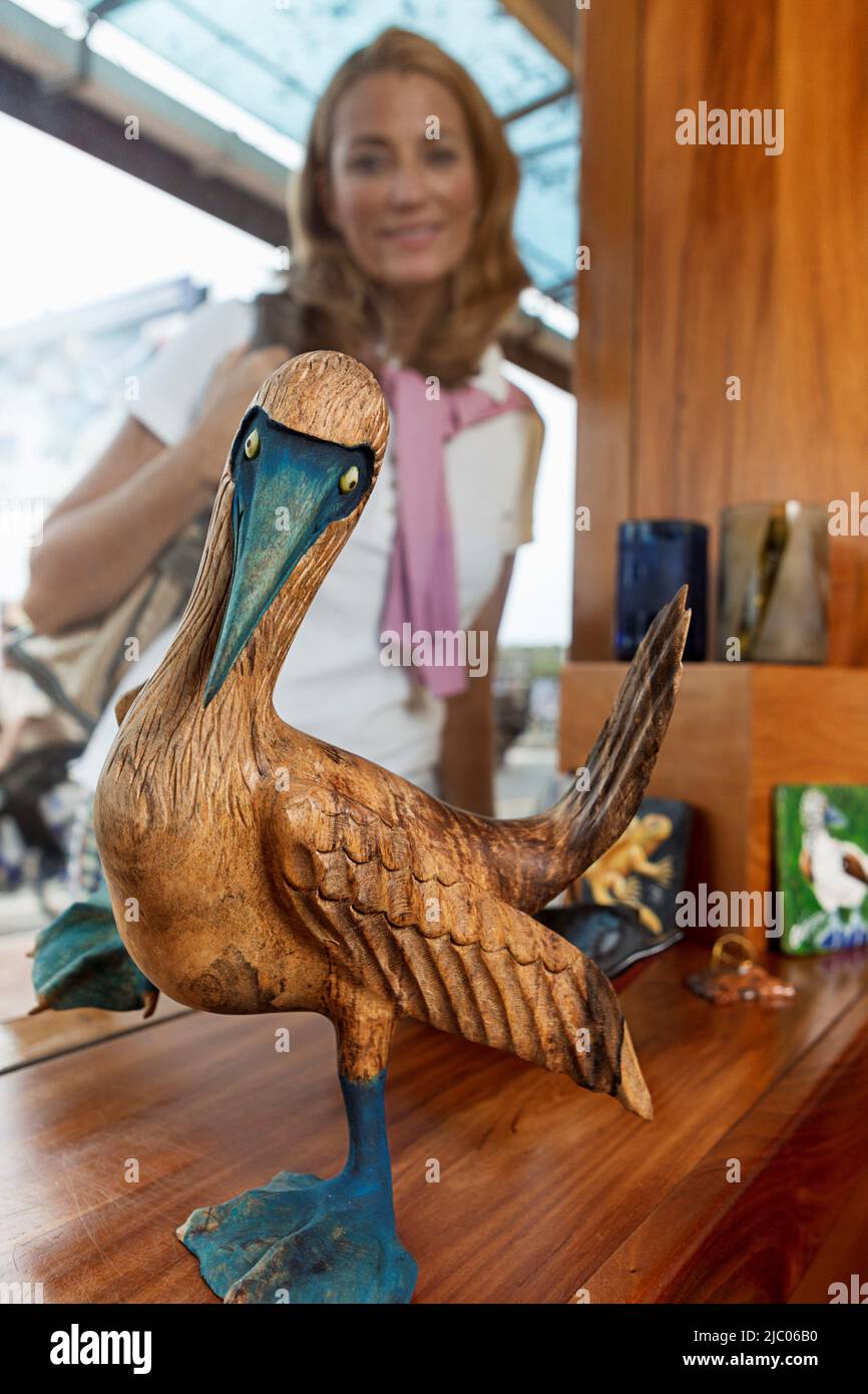 Equateur, Îles Galapagos, Booby à pieds bleus au comptoir à la boutique de souvenirs, femme en arrière-plan regardant la sculpture Banque D'Images