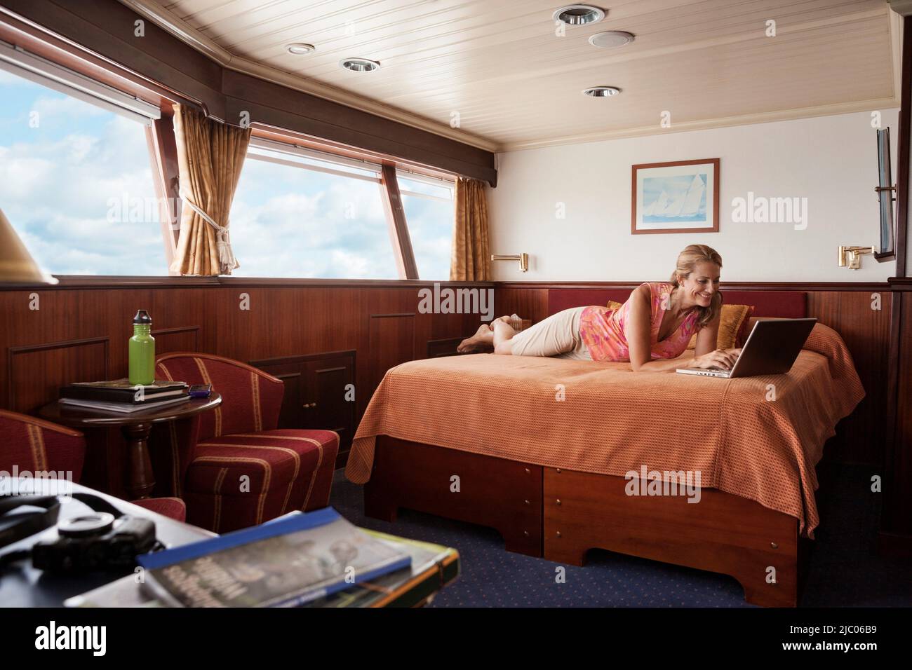 Femme couché sur le lit à l'aide d'un ordinateur portable dans la cabine du bateau de croisière voile mer Banque D'Images