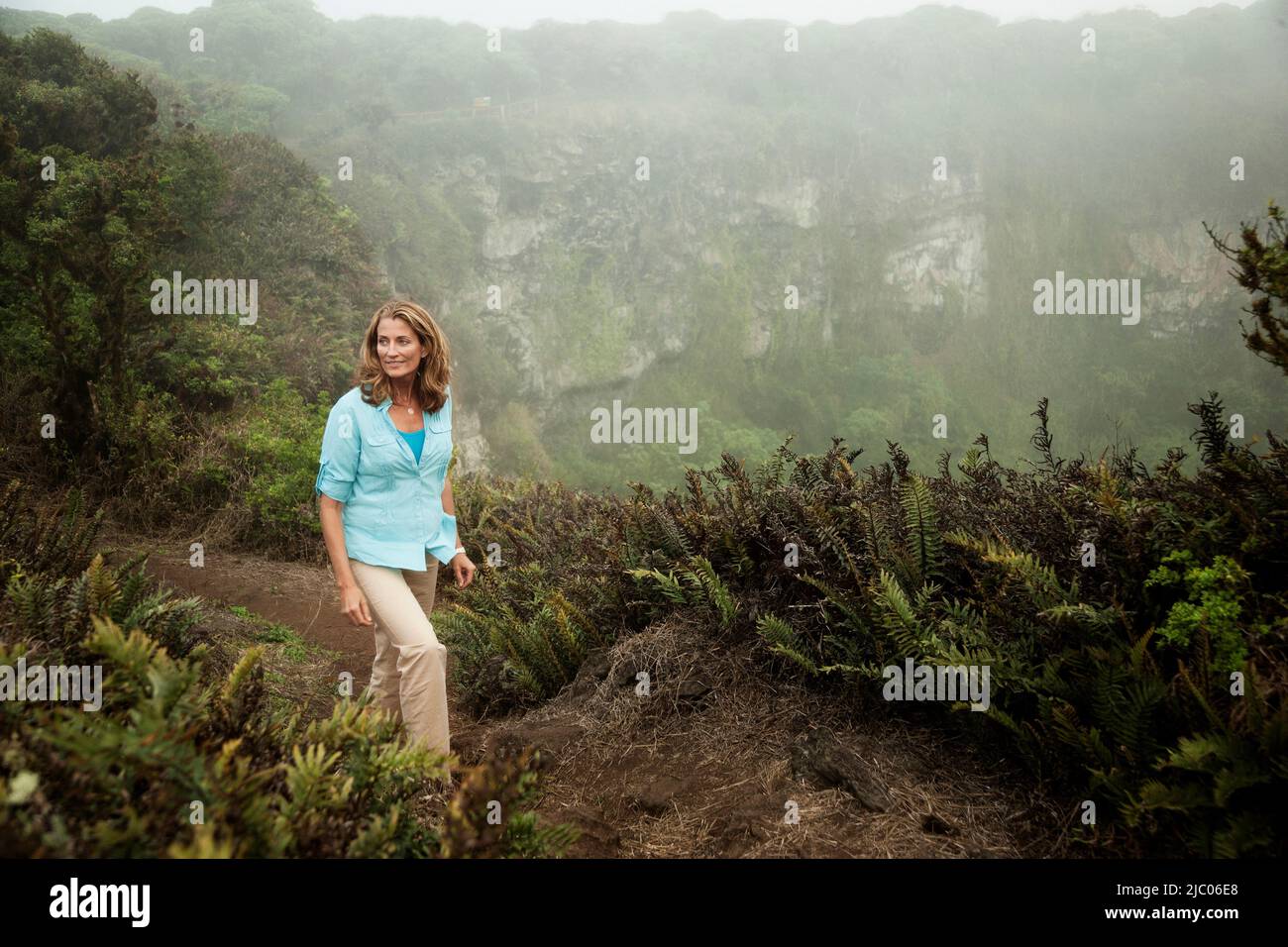 Equateur, îles Galapagos, femme marchant sur le sentier le long de la montagne luxuriante Banque D'Images