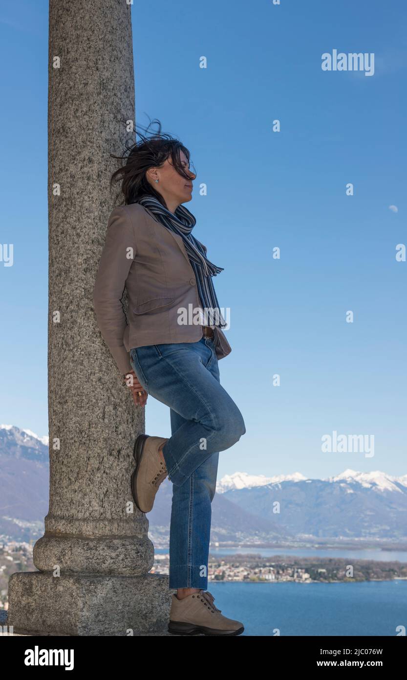 Femme penchée sur une colonne et profitez de la vue panoramique sur le lac alpin majeur avec la montagne enneigée à Ascona, en Suisse. Banque D'Images