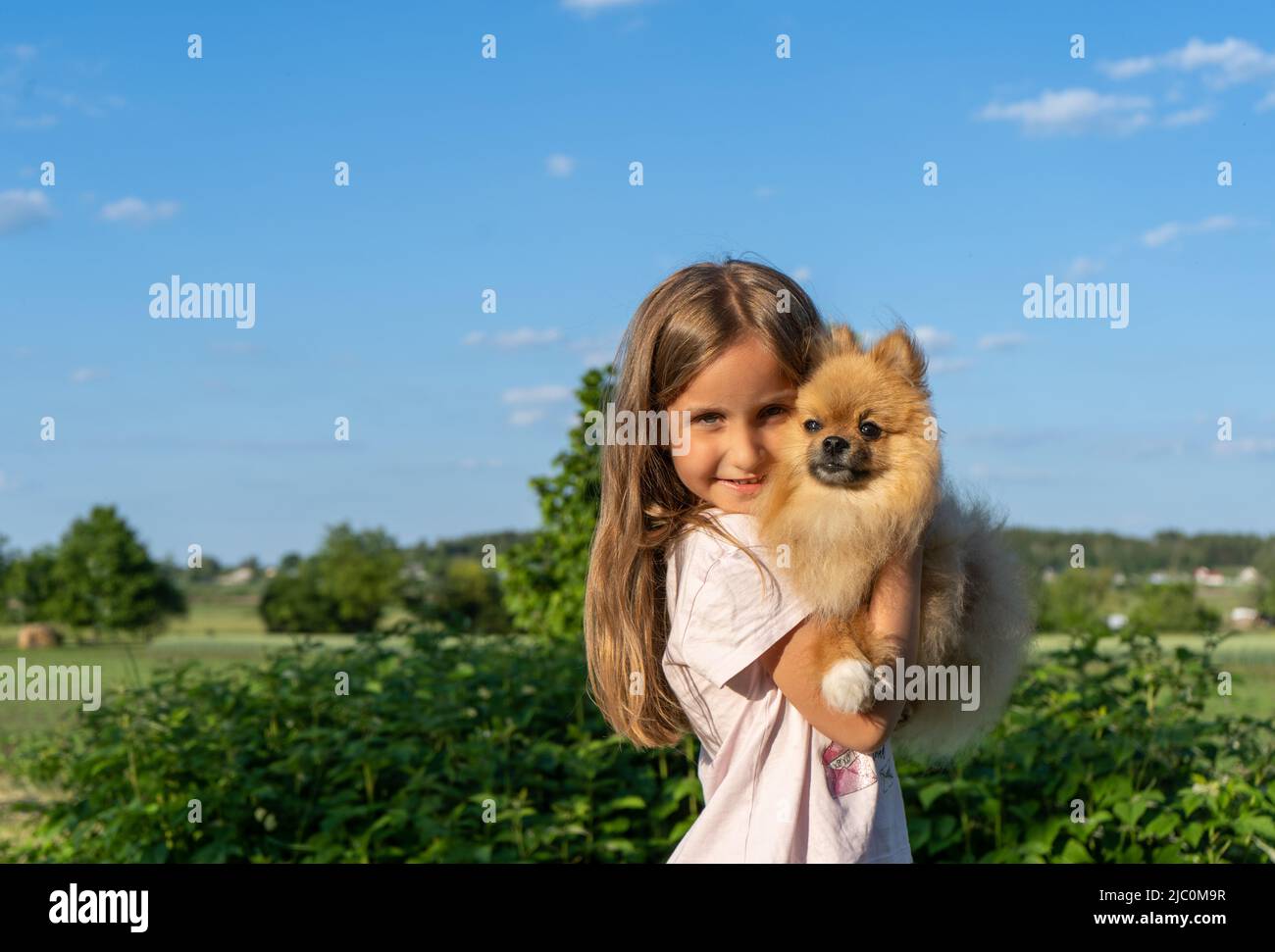 Petite fille tenant un petit chien mignon dans ses bras. Marchez avec votre animal de compagnie un jour d'été Banque D'Images