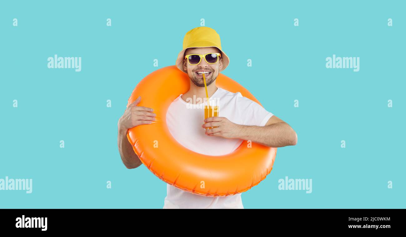 Joyeux jeune homme avec un cercle de natation gonflable et avec un verre de jus aime les vacances d'été. Banque D'Images