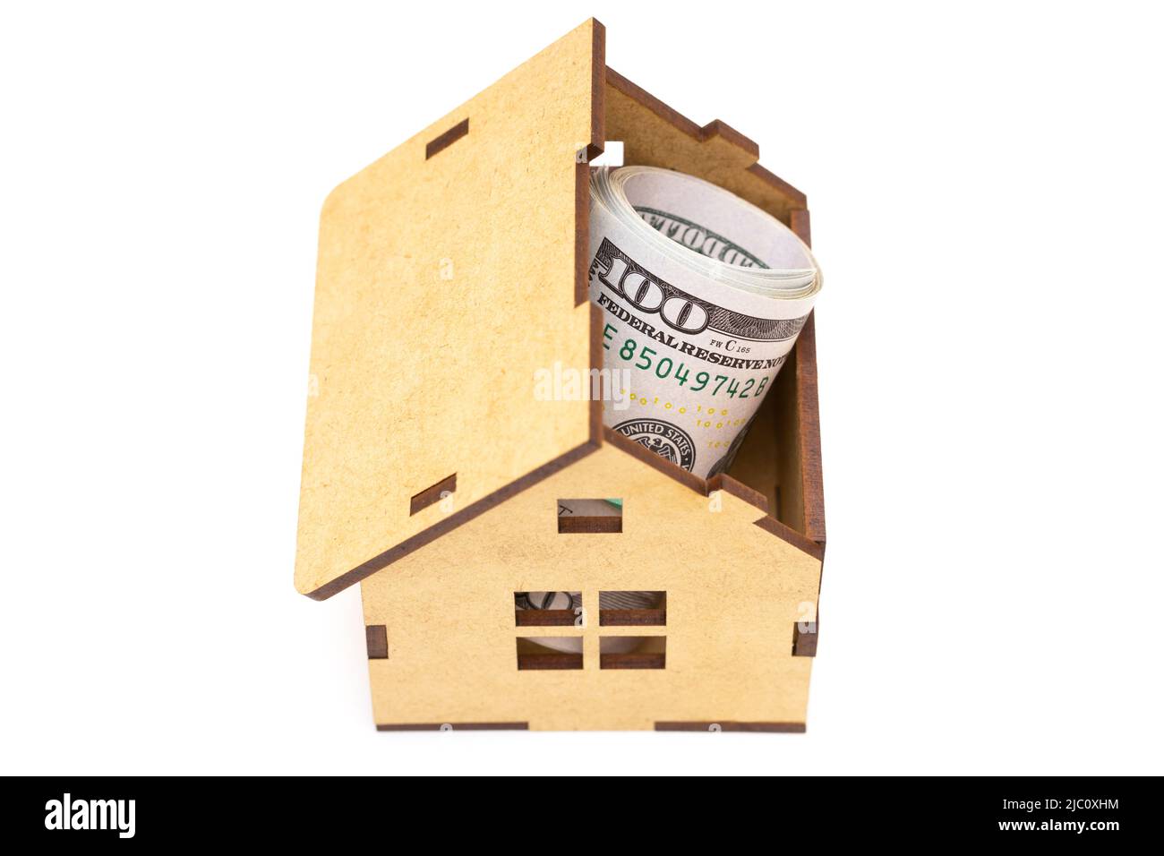 Des billets de cent dollars roulent à l'intérieur d'une maison en contreplaqué de jouet isolée sur fond blanc. Concept de dépôt hypothécaire. Banque D'Images