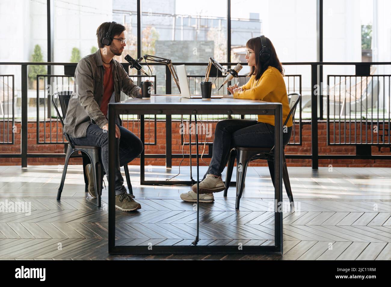 Les baladodiffusions homme et femme dans les écouteurs se interviewent pour le podcast audio en studio. Deux créateurs de podcast parlent tout en enregistrant un podcast ensemble. Diffusion en direct. Vue latérale Banque D'Images