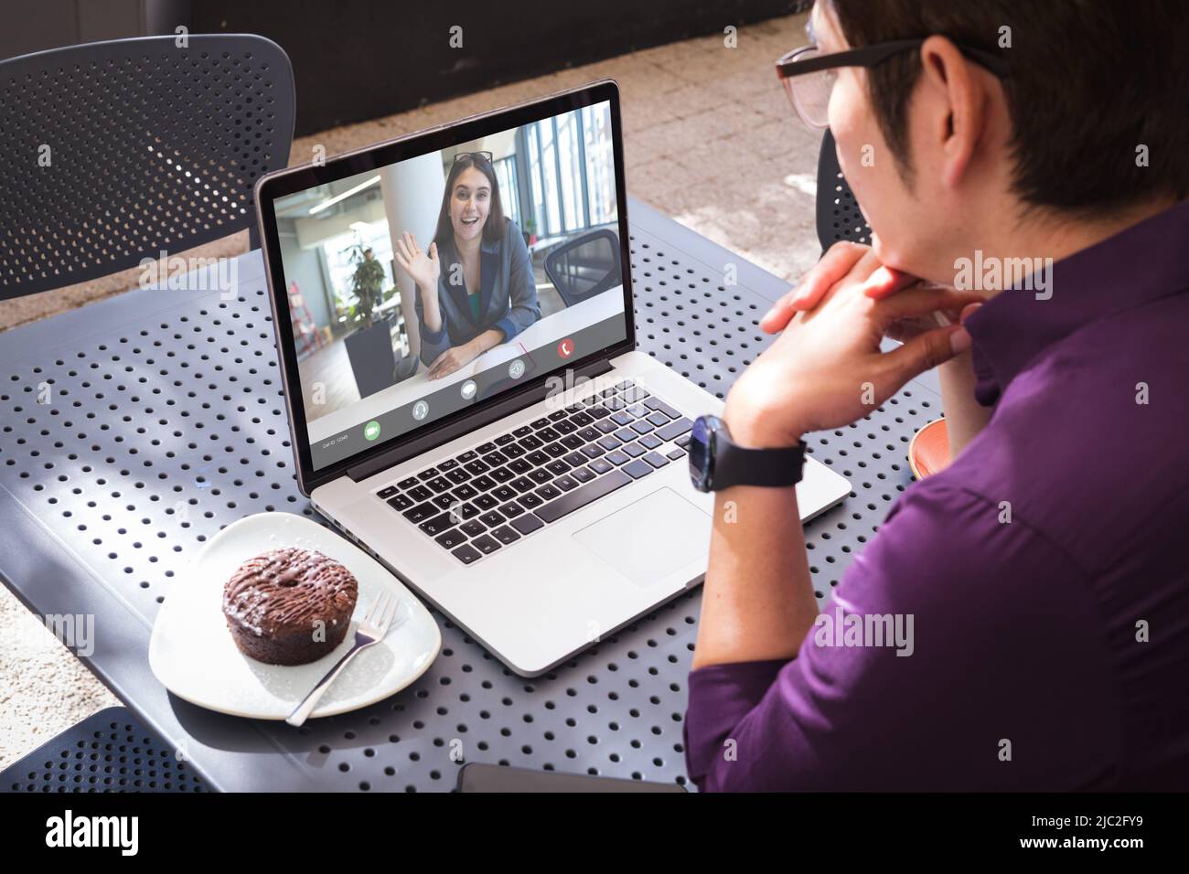 Bonne femme d'affaires caucasienne, qui agite la main sur la vidéo avec un collègue asiatique de sexe masculin assis dans un café Banque D'Images
