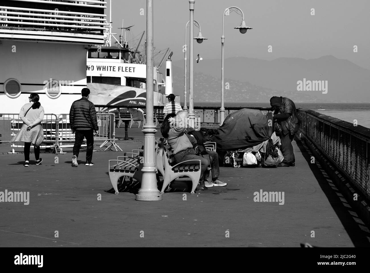 Les touristes marchent et s'assoient le long d'un quai où un homme sans abri a installé un camp de fortune dans la région de Fisherman's Wharf à San Francisco, en Californie. Banque D'Images